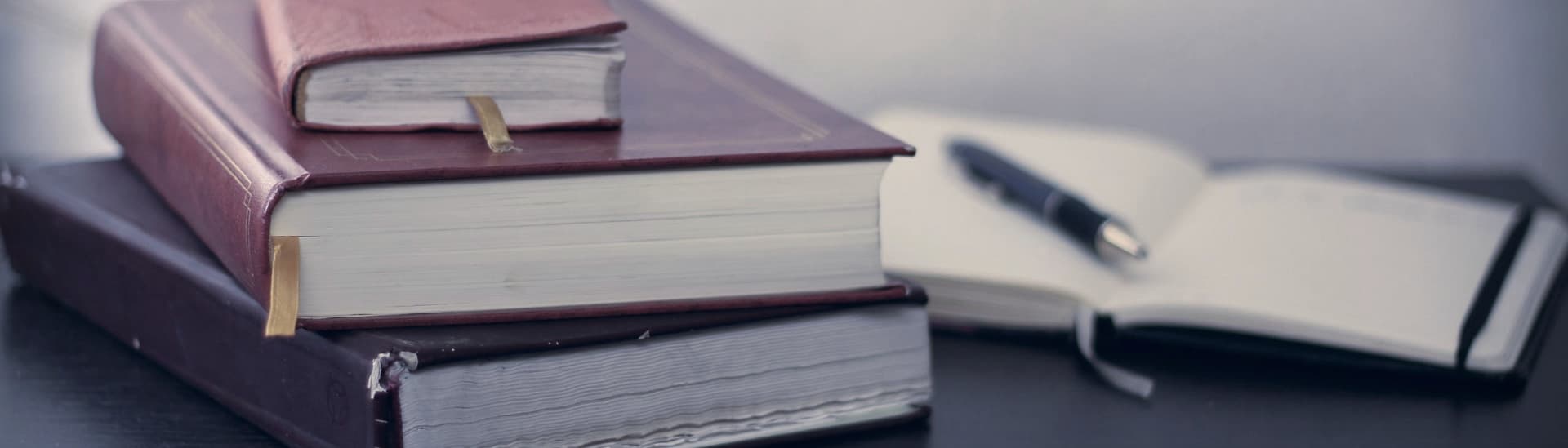 A stack of bound law books on a desk beside an open notebook and pen