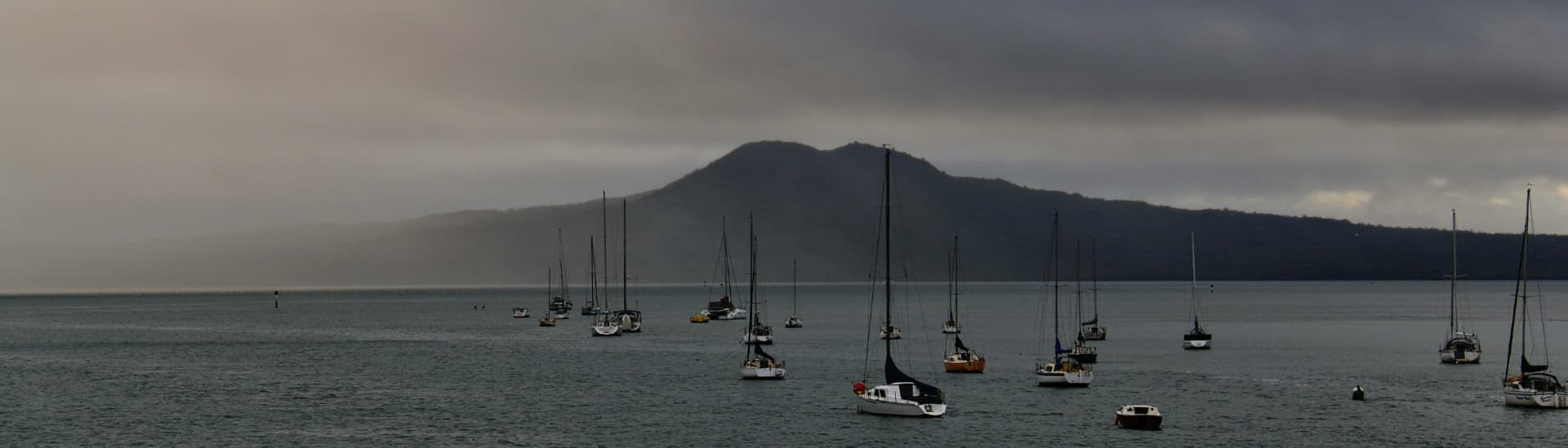 Yachts moored off Takapuna with Rangitoto Island beyond, under heavy cloud